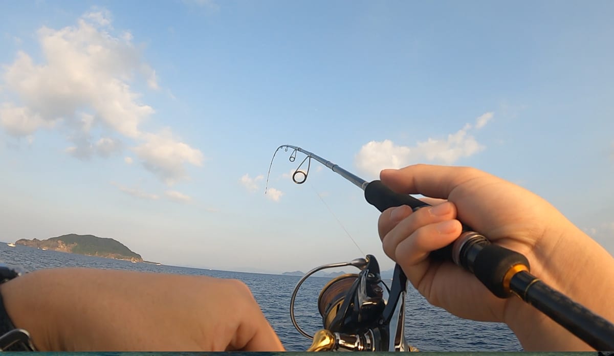 冠島周辺の船上でオモリグのロッドを持つ手元。キャスト後にシャクってステイで誘っているところ